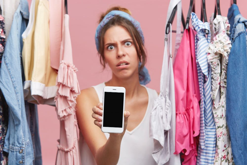 Shopper holding up a phone in frustration between clothing racks